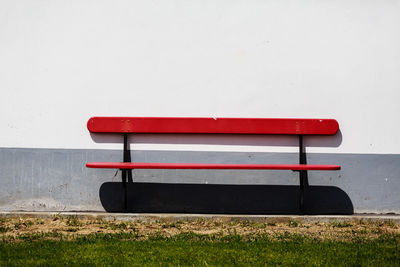 Empty bench on field against wall