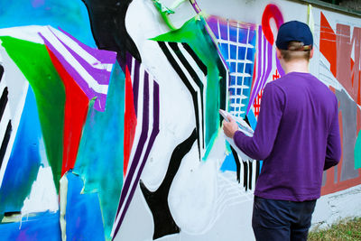 Rear view of man standing by graffiti wall