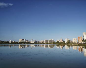 Reflection of buildings in lake against clear blue sky