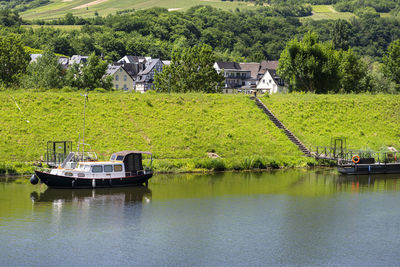 One motor boat moored in the marina on a calm river, forested hills are visible.