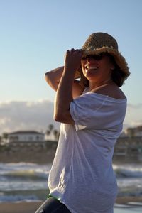 Side view of young woman standing against sea during sunset