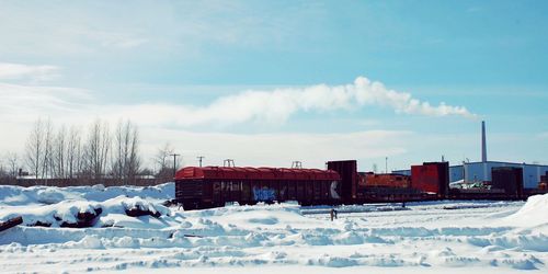 Freight train by snow covered field against cloudy sky