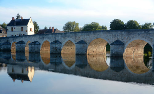 Arch bridge over river by buildings against sky