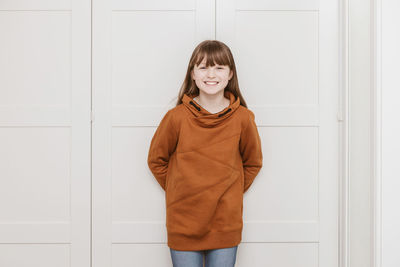 Portrait of a tein-haired girl 9 years old at home in a brown sweater, looking at the camera 