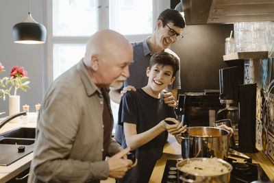 Smiling boy preparing food with grandfather and father in kitchen at home