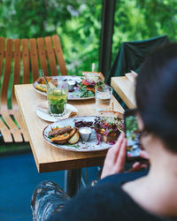 Rear view of woman photographing food on table at cafe