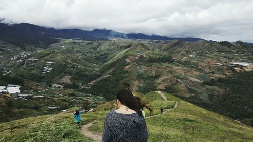 Rear view of woman walking on mountain against cloudy sky