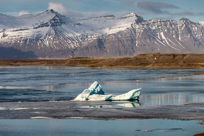 Frozen lake by snowcapped mountains against sky