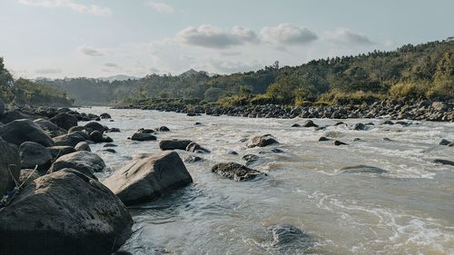 Scenic view of rocks by river against sky