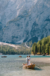 Man sitting in boat on lake against mountains