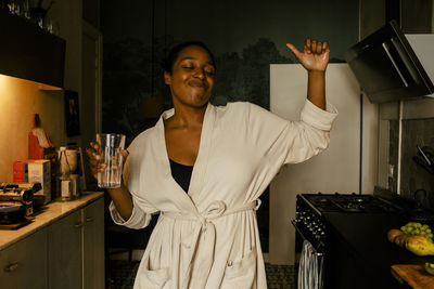 Carefree young woman holding drinking glass while dancing in kitchen at home