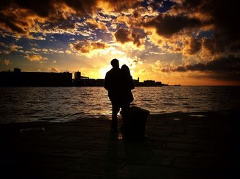 Silhouette couple at sea shore against orange sky