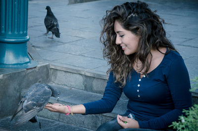 Young woman feeding pigeons while sitting on steps