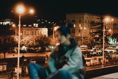 Woman sitting on illuminated street at night