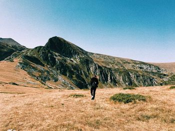 Rear view of man walking on mountain against clear sky