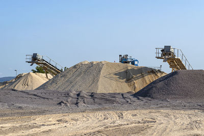 Conveyor belt over heaps of gravel against the blue sky at an industrial cement plant.