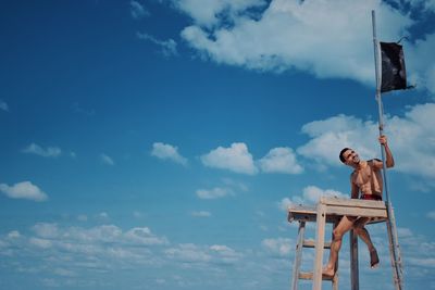 Low angle view of girl sitting on wood against sky