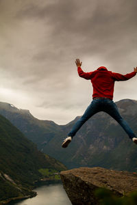 Man jumping over mountain against sky