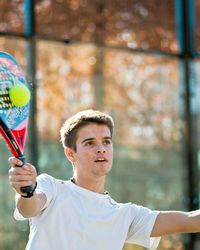 Young man looking away while hitting tennis ball