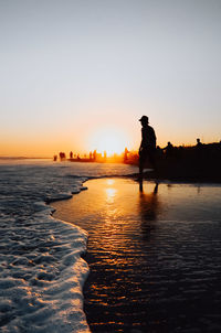 Silhouette man standing on beach against clear sky during sunset