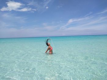 Woman tossing hair in sea against sky