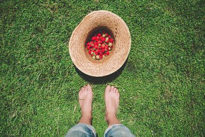 Barefoot woman standing next to straw hat full of strawberries on the lawn