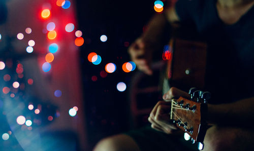 Midsection of man playing guitar by defocused lights