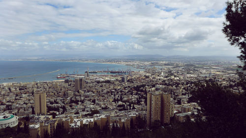 Aerial view of buildings and sea against cloudy sky in city