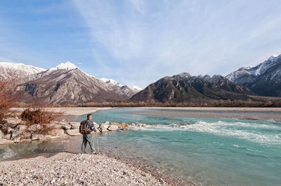 Rear view of man standing on rock by river against sky