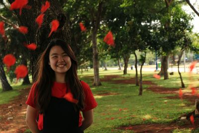 Portrait of smiling young woman standing against trees