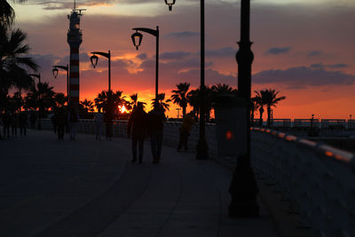 Silhouette people walking on footpath during sunset