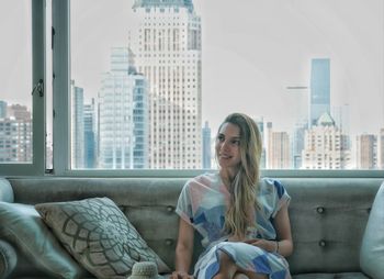 Young woman sitting on sofa against buildings in city