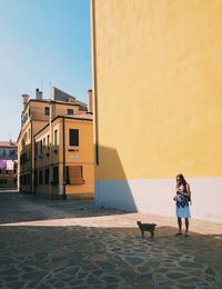 Woman standing next to building against sky with a cat