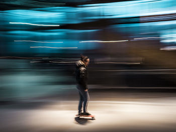 Blurred motion of woman skateboarding on street at night