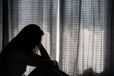 Side view of woman sitting against window at home