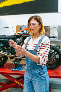 Female mechanic with security glasses touching transparent tablet