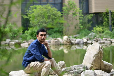 Young man sitting on rock against trees