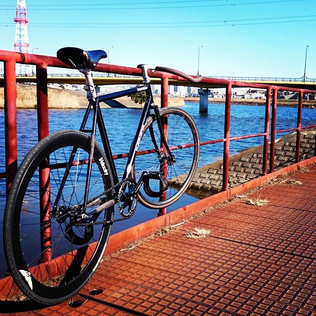 railing, clear sky, transportation, bicycle, water, built structure, mode of transport, blue, architecture, metal, river, sunlight, sea, day, outdoors, bridge - man made structure, shadow, sky, connection, copy space