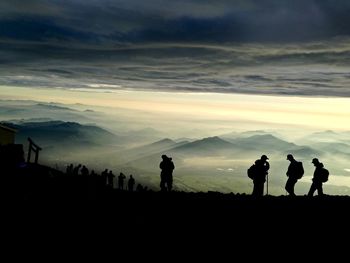 Silhouette people walking on mountain against sky during sunset