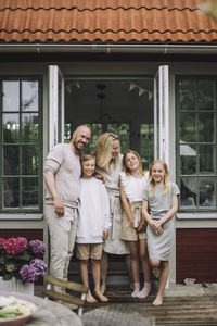 Portrait of happy family standing together against doorway on porch