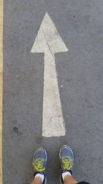 Low section of man standing by arrow symbol on road