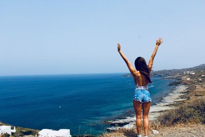 Woman with arms raised standing at beach against clear sky