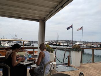 Rear view of people sitting on harbor against sky