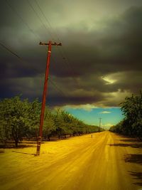 Road passing through field against cloudy sky