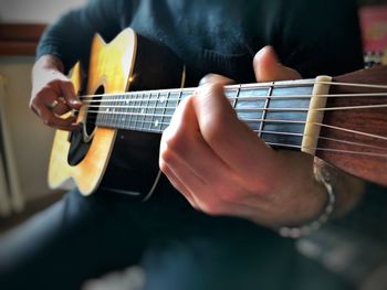 Midsection of man playing guitar while sitting at home