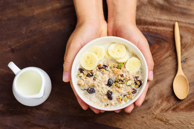 Cropped hands of woman holding breakfast in bowl on wooden table