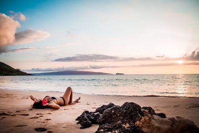 Woman lying on beach against sky