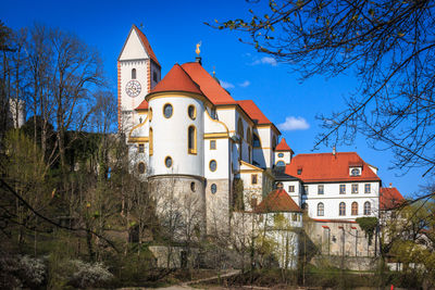 Low angle view of buildings and trees against blue sky