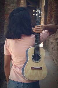 Rear view of woman holding acoustic guitar in alley