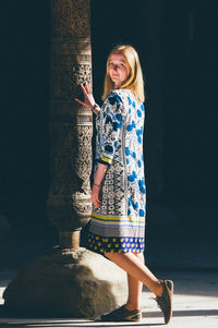 The blond girl standing near the old ancient  column. touch eternity